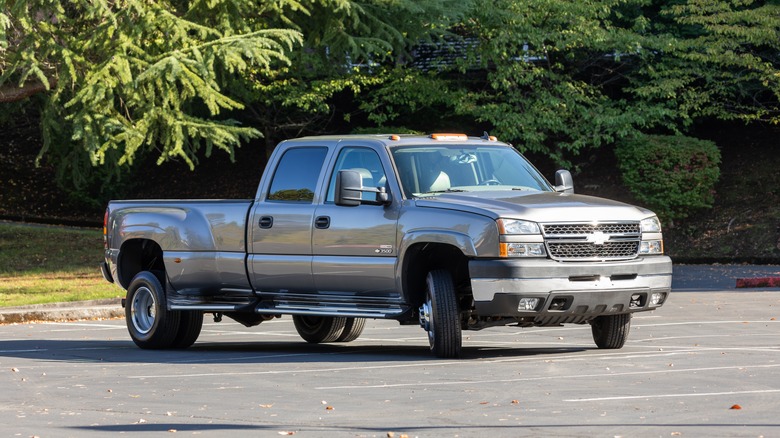 Silver Chevy Silverado dually in parking lot with trees behind