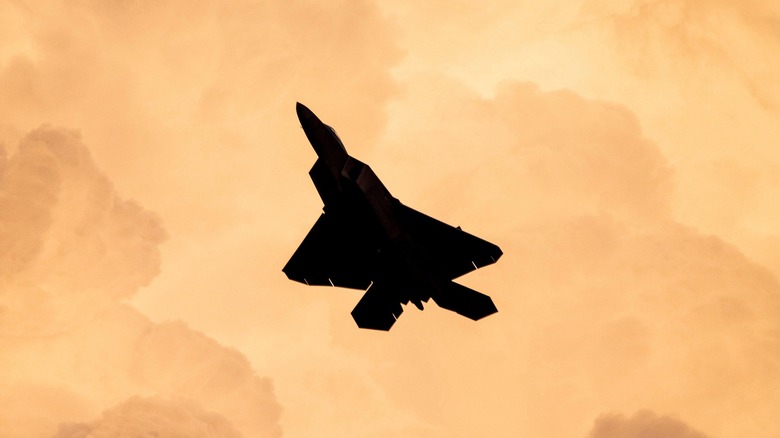 The silhouette of an F-22 Raptor flying at twilight among clouds