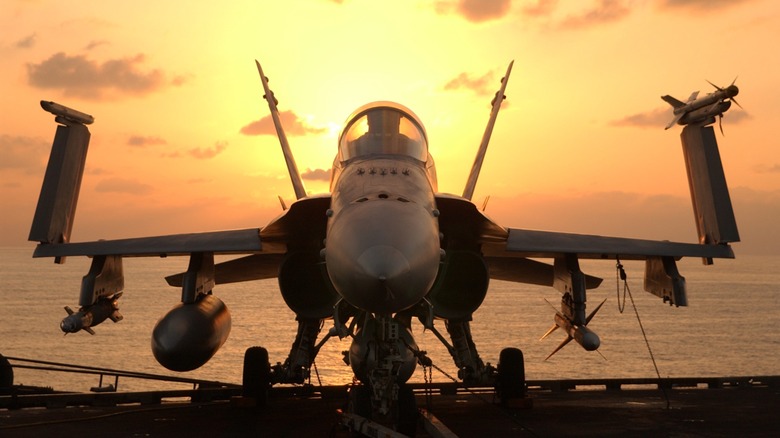 An F/A-18 Super Hornet loaded with weapons on an aircraft carrier flight deck