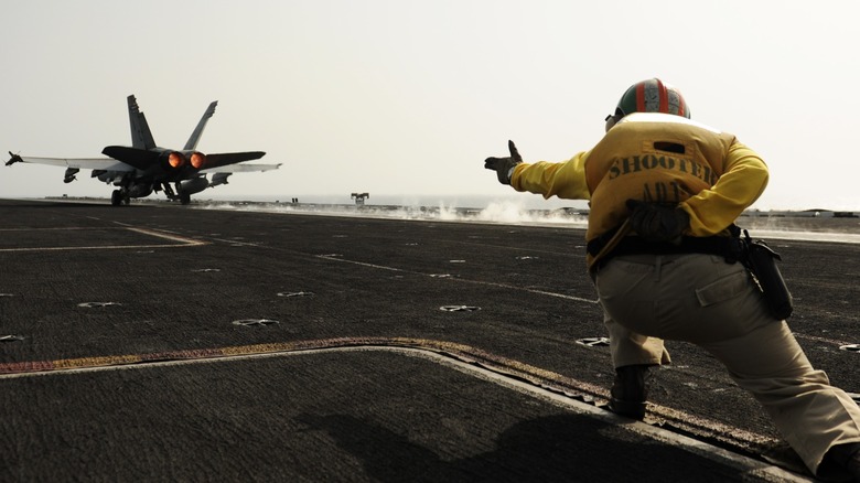 A flight deck shooter launching an F/A-18C Hornet off the deck of an aircraft carrier