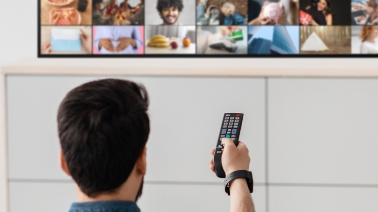 Person holding remote control with television in the background.