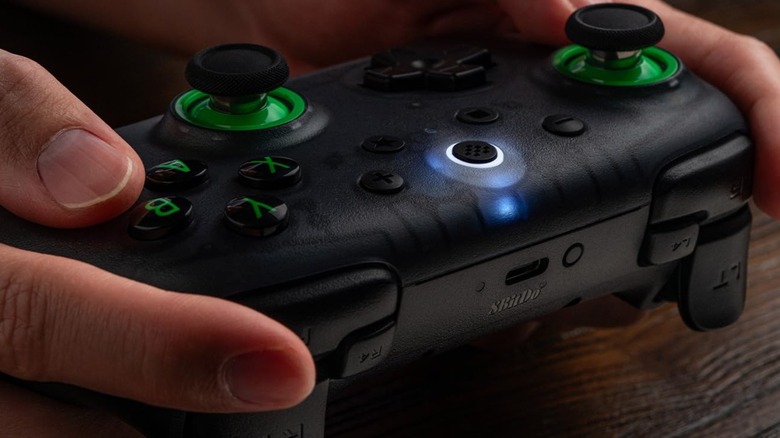An 8BitDo Ultimate 2C gaming controller being held by a person showing its logo and charging port