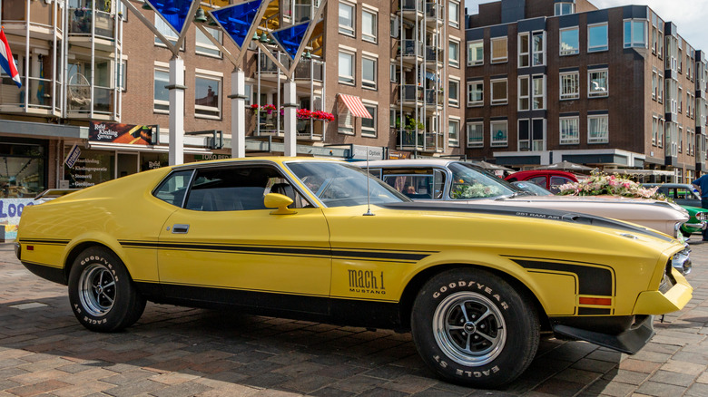 A classic yellow Mustang Mach 1 parked in a display, equipped with Goodyear tires.