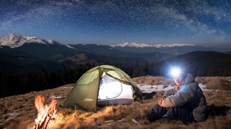 Man sitting next to tent with headlamp on