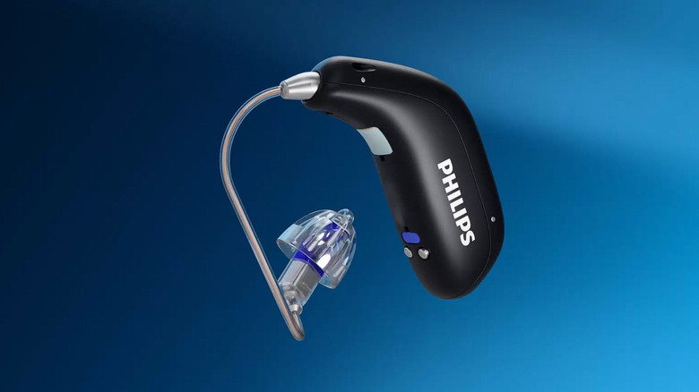 A 3D model of a black Philips hearing aid of the behind-the-ear category suspended in air against a blue background.