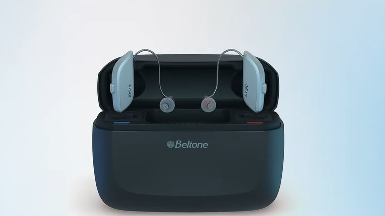 A pair of white Beltone hearing aids hovering above their airpods-like charging case, finished in black.