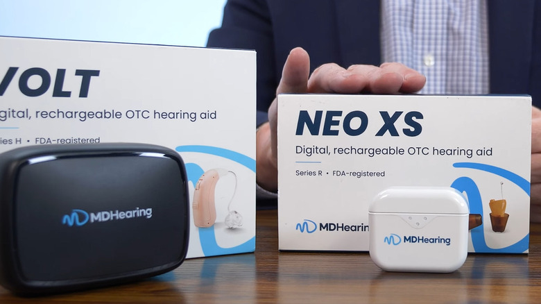 Two sets of brand-new, recently unboxed MDHearing Hearing aids sitting on a table with their respective boxes.