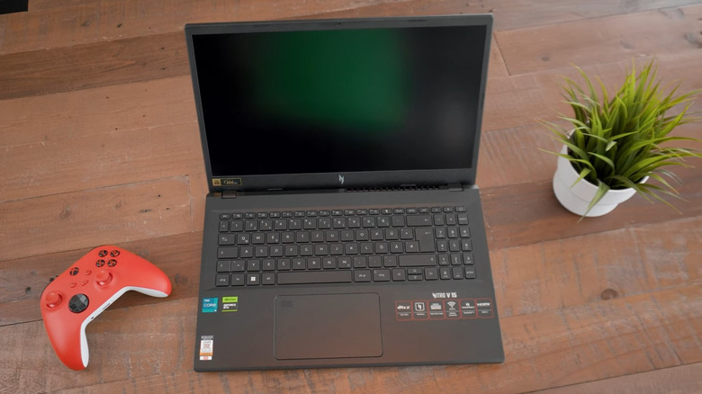 Acer Nitro V on wood table in between plant and game controller