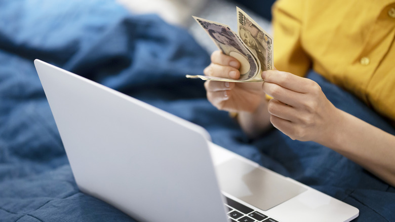Woman counting money while looking at laptop