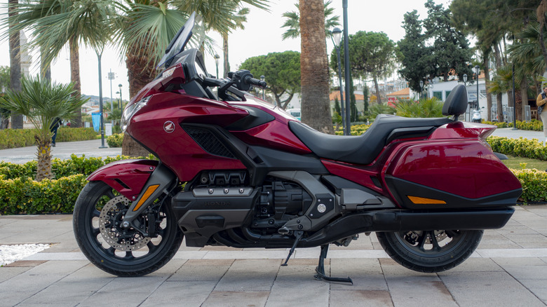 A red Honda Gold Wing parked at the side of a paved section of walkway in the afternoon.