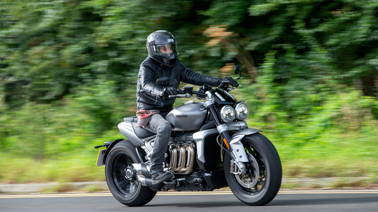 A motorcyclist in full kit zooming down a country road on a Triumph Rocket 3 R