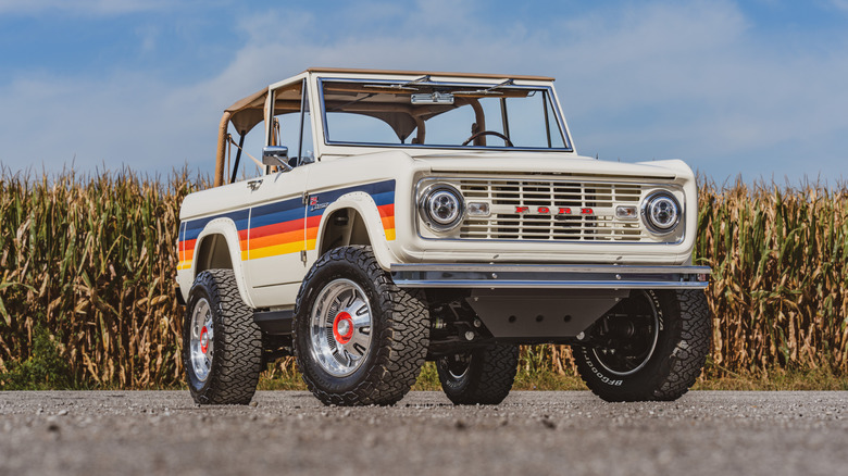 A restomod first-generation Ford Bronco parked in front of a corn field.