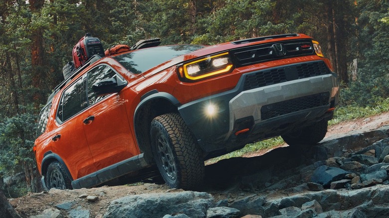 An Orange Sunset Honda Passport driving on a hill over small rocks