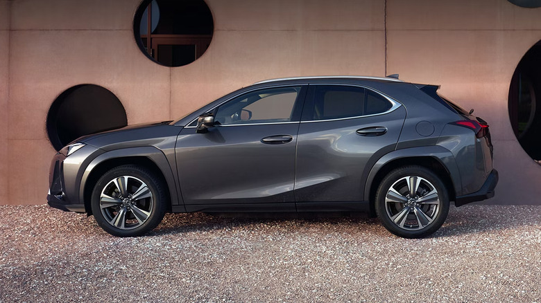 A Lexus UX parked on gravel near a wall with holes