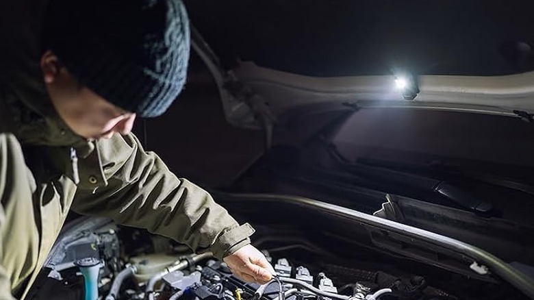 A man using flashlight under car hood