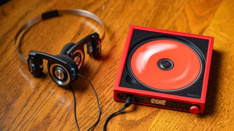 Red FiiO DM15 on a wooden table next to a pair of Koss PortaPro headphones.
