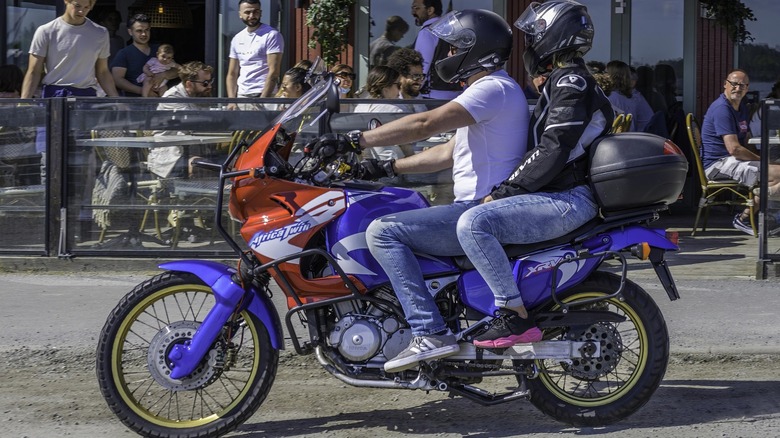 A couple riding an older Honda Africa Twin adventure bike two-up.