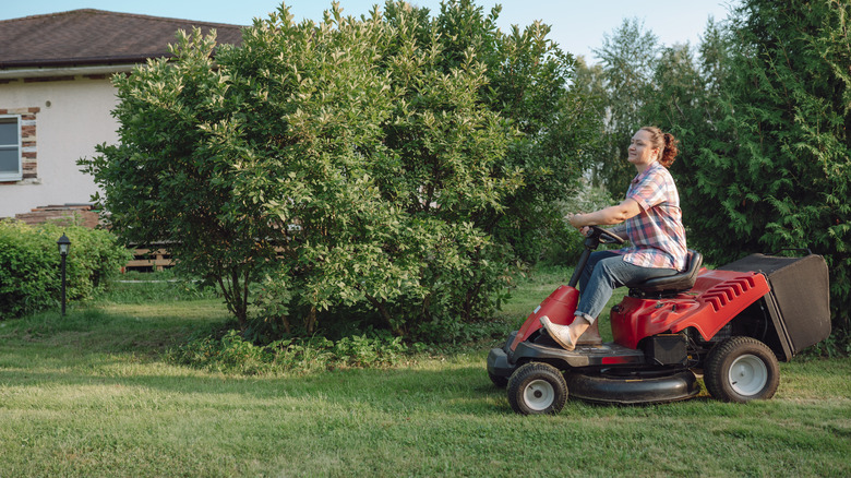 A woman using a riding lawn mower on a large lawn.