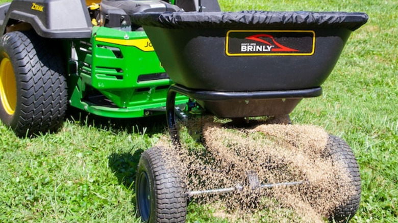 A tow-behind spreader by Brinly attached to a riding mower.