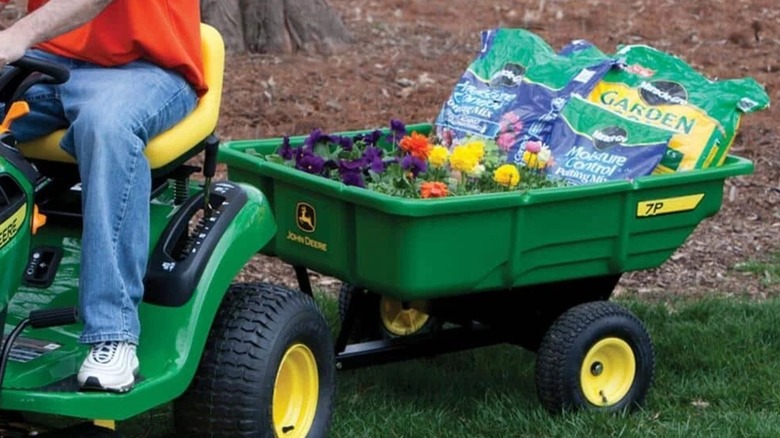 A driving lawn mower with a cart by John Deere attached.