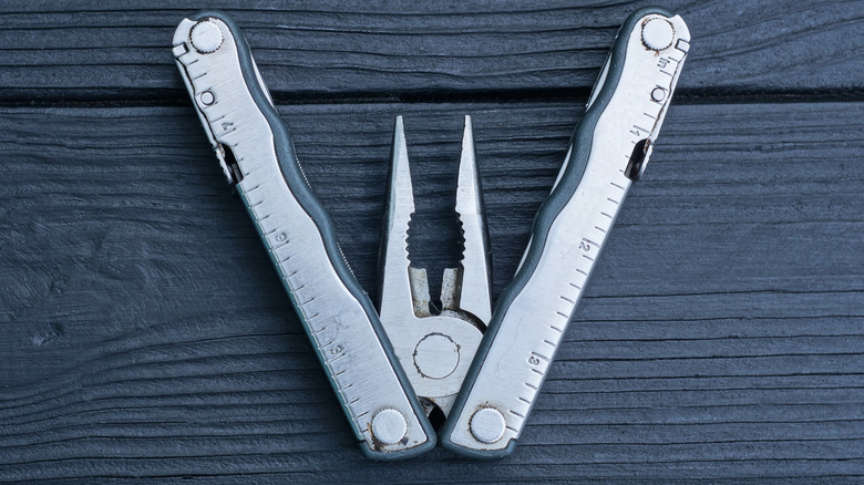 Silver multi-tool with pliers partially out, upside-down, on a black wood background