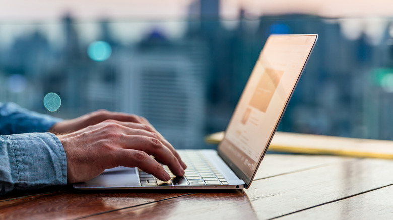 A person typing on a laptop, a cityscape view in the background