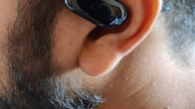 Closeup of a person's ear wearing a pair of black open ear earbuds