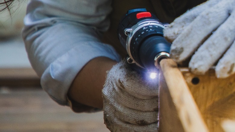Power screwdriver held by human hands near wood.
