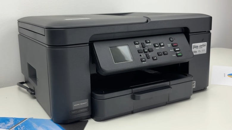 Brother MFC-J1360DW printer on a white table with printed material around it
