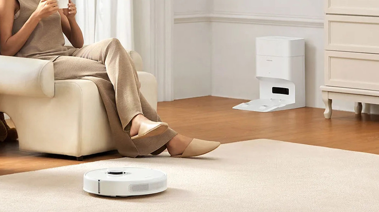 Dreame D10 Robot Vacuum working on a carpet while a woman watches from her chair.