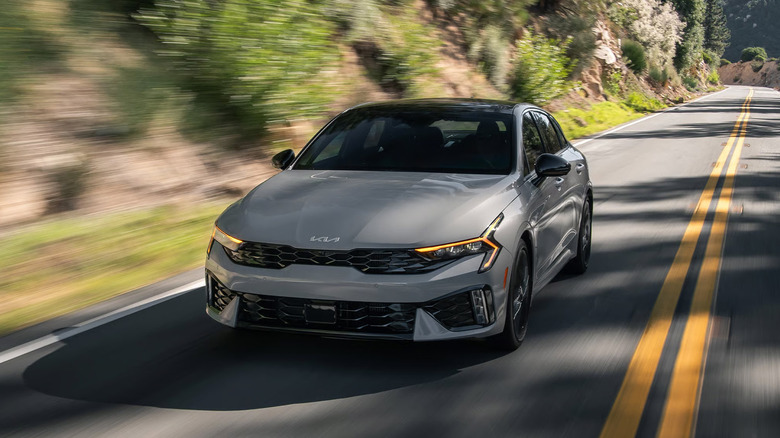 A front end shot of a gray 2026 Kia K5 driving
