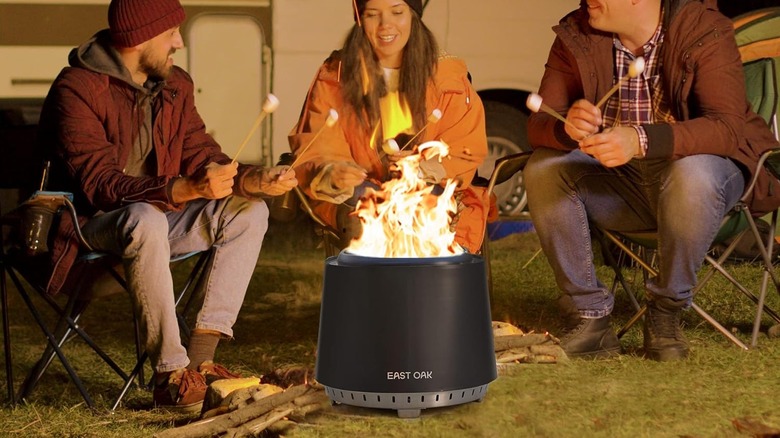 East Oak Fire Pit around a small camp ground with three people holding marshmallows with a camper in the background