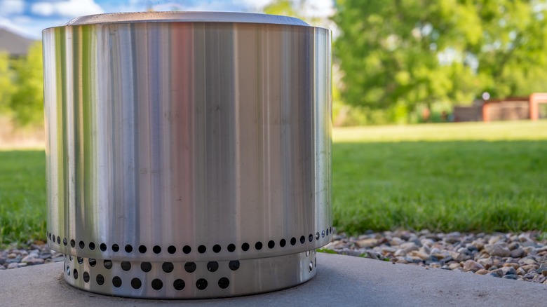 Steel smokeless fire pit on concrete with a backyard in the background