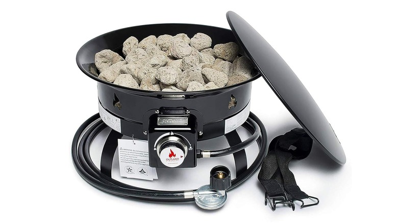 Black Outland Fire Pit with lava rocks and hose wrapped around it, cover on side on a white background