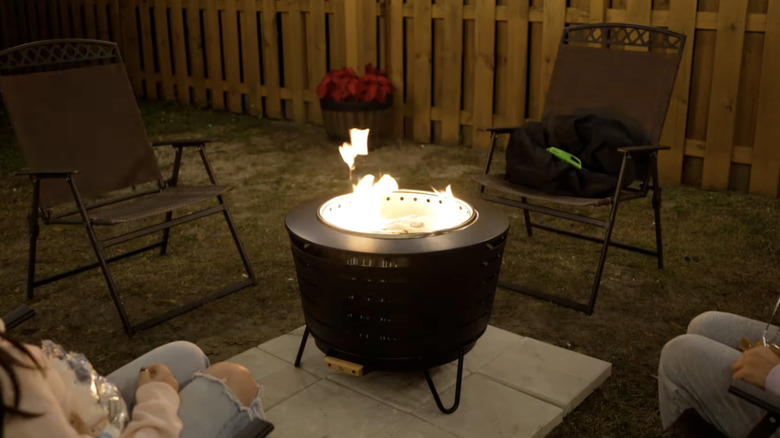 Black fire pit with a fire roaring at the center in a backyard