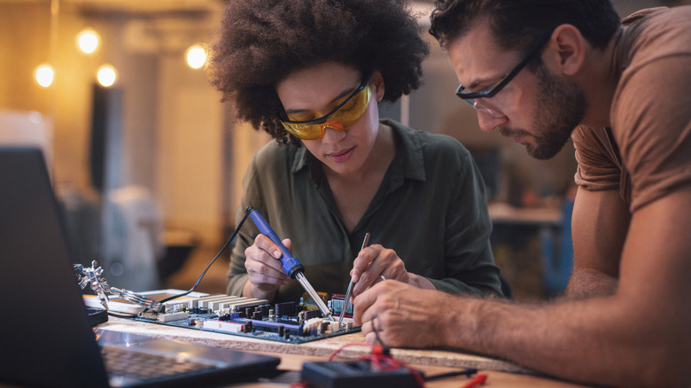 two people soldering electronic components