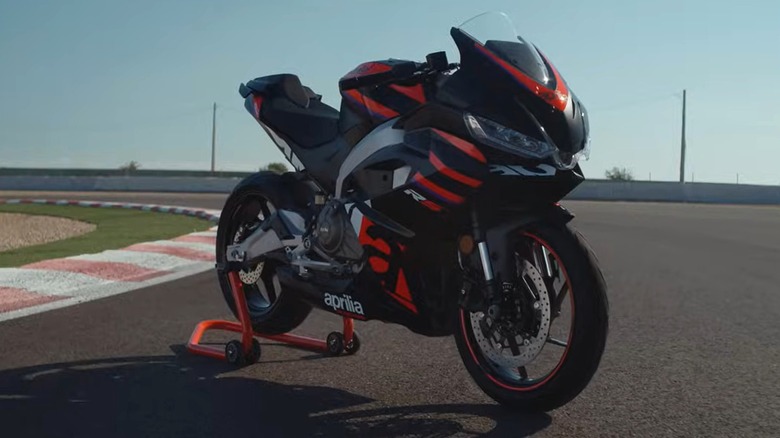 An Aprilia RS 457 sportbike sits on a racetrack stand, looking aggressive and track-ready under the bright sun.
