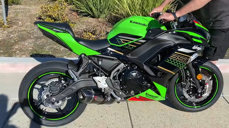 A vibrant green Kawasaki Ninja 650 is being held upright on the sidewalk, showing off its sharp fairings and bold graphics.