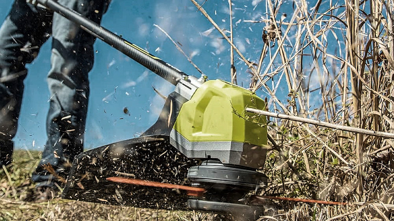A man trimming thick brush with a Ryobi string trimmer.