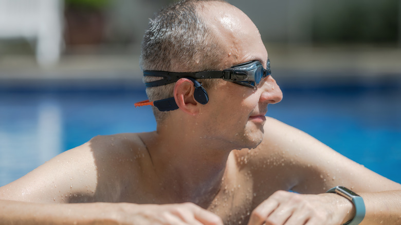 A man wearing goggles and bone conductor headphones at the side of a swimming pool