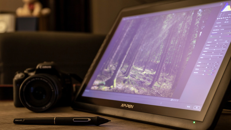 XP-Pen tablet, showing an image of trees, next to a stylus and a camera.