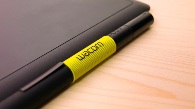 A Wacom stylus on a wooden table next to tablet.