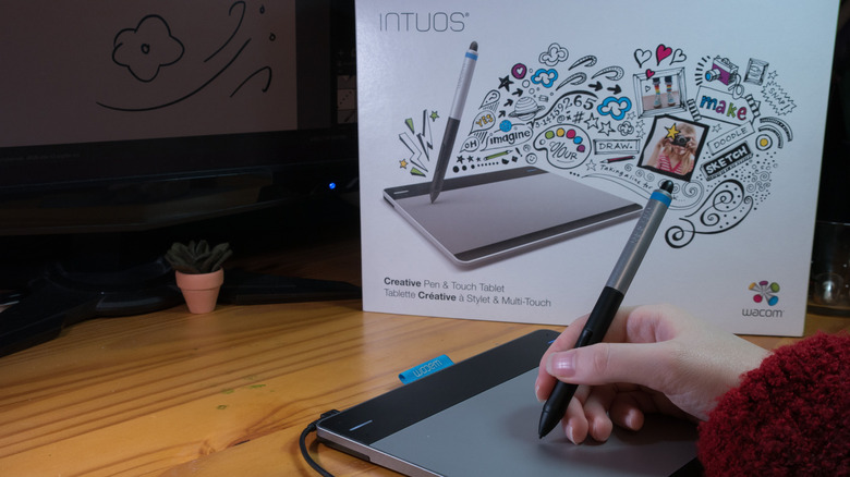 Hand using a stylus on a Wacom Intuos tablet, Intuos box in the background.