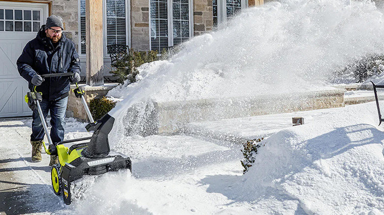 A man using a Ryobi snow blower to clear his driveway