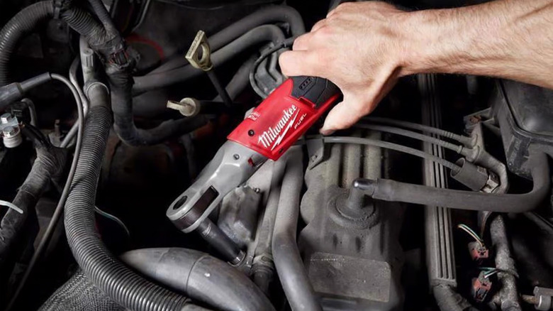 A person using a Milwaukee cordless ratchet on a car engine