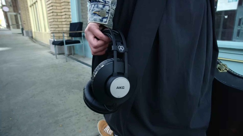Close-up of a woman walking on a sidewalk carrying AKG K72 headphones