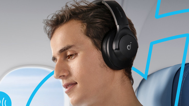 Close-up of a person sitting in an airline seat wearing Anker Soundcore Q20i headphones