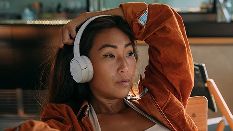 Woman sitting in a wooden chair and wearing a pair of JBL Tune 520BT headphones