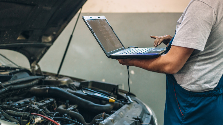 Man standing in front of open car engine bay with laptop