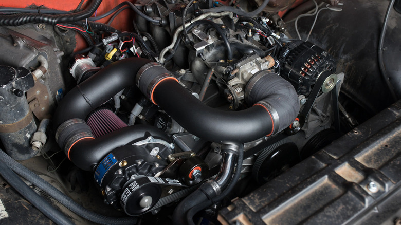 A close-up of an older car's orange engine bay featuring a supercharged LS-based V8.